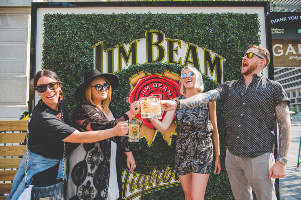 People smiling and cheering in front of a jim beam sign
